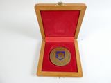 une image représentant une médaille d'or dans un coffret en bois posé sur une surface blanche