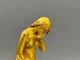 statue en or représentant une femme assise sur un rocher, la main posée sur le menton