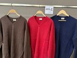 trois pulls suspendus à un portant dans un magasin de vêtements