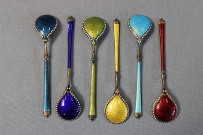 six spoons with different colors are lined up on a gray surface