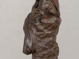 bronze statue of a woman sitting on a rock with her hands on her knees