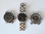 three watches are sitting on a white surface, one is black and the other is silver