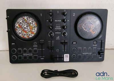 un gros plan d'un contrôleur de DJ posé sur une table à côté d'un chargeur