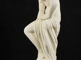 white marble statue of a woman sitting on top of a ball