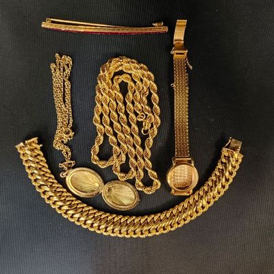 un gros plan sur un collier, un bracelet et une montre en or posés sur une surface noire
