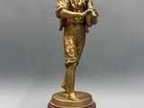 une figurine antique en bronze représentant un garçon tenant un oiseau, posée sur un socle en marbre