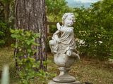 une statue représentant une femme assise sur un socle dans un jardin