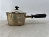 une vieille saucière en argent avec une poignée noire, posée sur une table