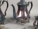 three silver teapots and two silver cups on a table