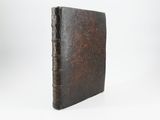 an old book with a brown cover sitting on a white surface