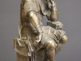 bronze statue of a man sitting on a stool with a book