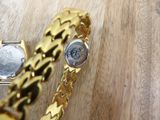 a gold bracelet and a watch on a wooden table