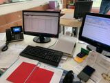 a desk with a computer, keyboard, phone and other items on it