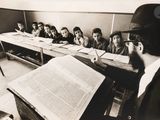 black and white photograph of a man reading a book in a classroom