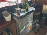 un petit réfrigérateur dans un coin d'une pièce où le sol est encombré d'objets