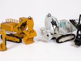 trois engins de chantier miniatures sont alignés sur une surface blanche