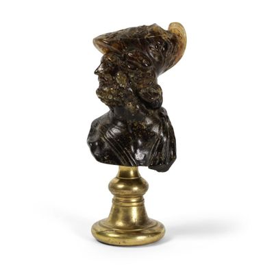 un buste antique en bronze représentant un homme coiffé d'un chapeau, posé sur un socle