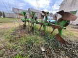 une charrue verte posée dans l'herbe à côté d'un bâtiment