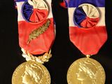 two gold medals on a black table with a red, white and blue ribbon