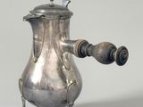 une cafetière en argent avec une poignée en bois, posée sur un socle