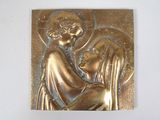 une photo représentant une plaque métallique sur laquelle figure l'image d'une femme tenant un enfant dans ses bras