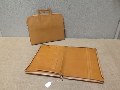 une mallette et un portefeuille en cuir beige posés l'un à côté de l'autre sur un lit