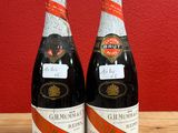 two bottles of wine sitting on top of a wooden table next to a red wall