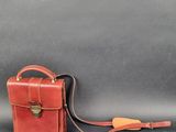 an old red leather briefcase with a strap and a handle