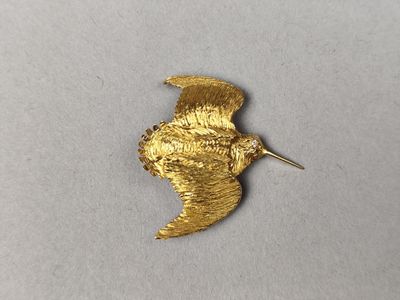 un gros plan d'une broche en forme d'oiseau dorée posée sur une surface blanche