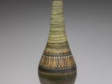 un vase vert et marron posé sur une surface blanche