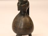 une petite figurine en bronze posée sur une surface blanche