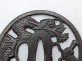 a black iron tsuba with a dragon and a fish on it