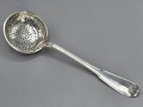 une cuillère en argent avec un manche, posée sur une surface grise