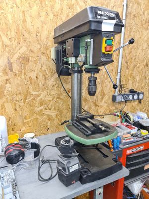 une perceuse posée sur un établi sur lequel se trouvent de nombreux outils