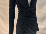 La robe est noire, à manches longues et avec un décolleté en V.