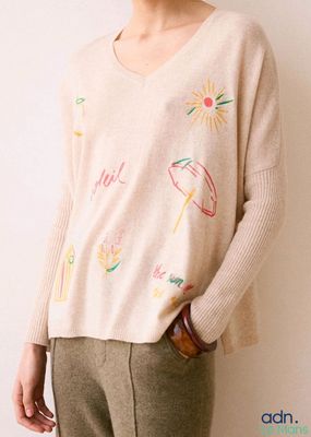 une photo d'une femme debout devant un mur blanc, vêtue d'un pull