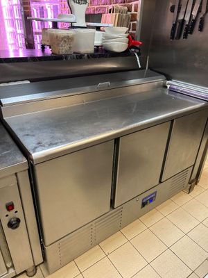 un grand plan de travail en inox dans une cuisine où des couteaux sont accrochés au mur