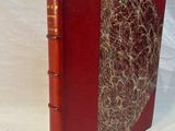 an old book with a red cover sitting on a white surface