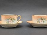 two cups and saucers with floral designs on them sitting on a table