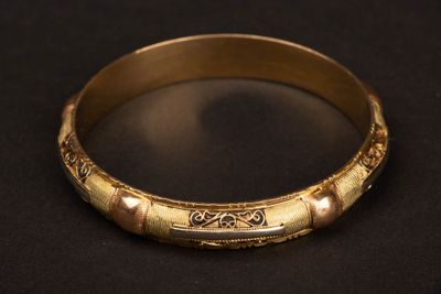 gros plan d'un bracelet en or sur une surface noire