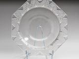 une assiette en verre transparent posée sur un support métallique, sur une table