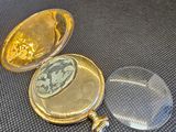 une montre de poche en or posée sur une table, à côté d'une loupe