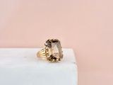 a gold ring with a smoky quartz stone on top of a white marble block