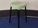 un tabouret vert posé sur un tapis bleu devant un mur blanc