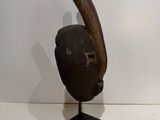 an old wooden mask on a metal stand on a white surface