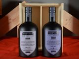 two bottles of wine sitting in a wooden box on a red cloth