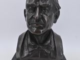 statue représentant le buste d'un homme portant un nœud papillon, posée sur un socle en marbre