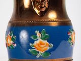 a blue vase with a gold handle and a rose design on it