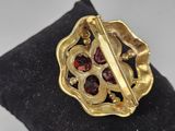 an image of a gold broochle with garnets on a black pillow