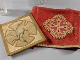 two pieces of cloth on a table with a glass in the background